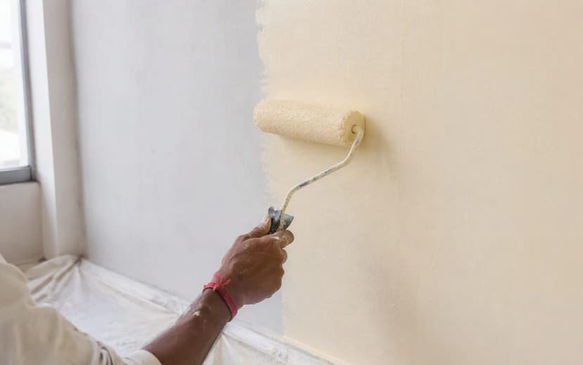 Painter applying cream emulsion paint with a roller on an interior wall